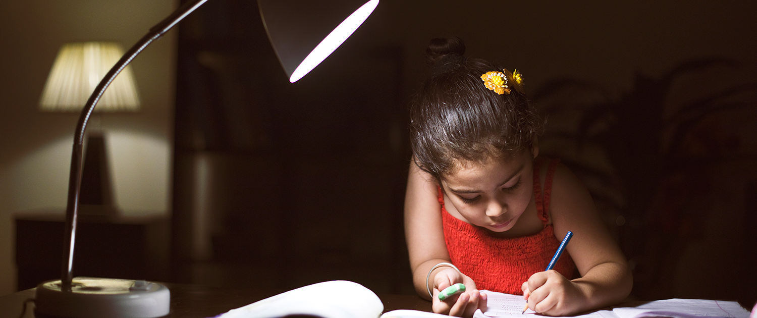 Energy equity child at table doing homework by light of a desk lamp