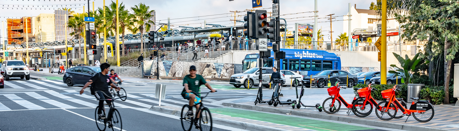 A busy intersection in downtown Santa Monica, with cyclists, e-bikes, scooters, electric buses, metro, and electric vehicles.