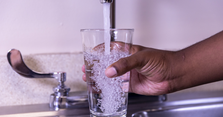 Someone holding a glass of water under a running faucet.