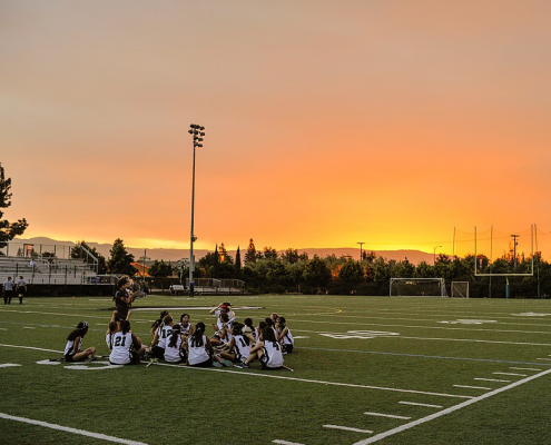 Student athletes sit on artificial turf football field at sunrise