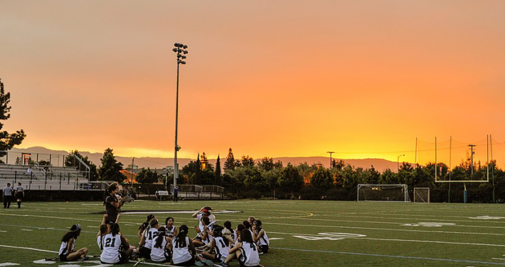 Student athletes sit on artificial turf football field at sunrise