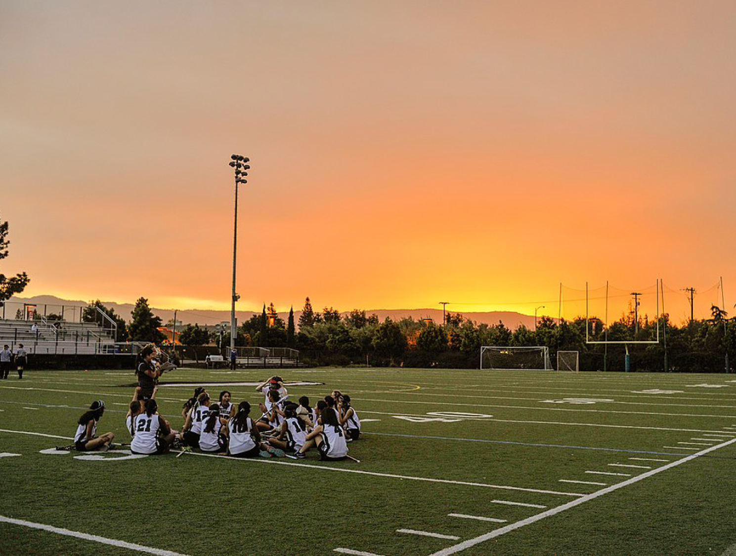 Student athletes sit on artificial turf football field at sunrise