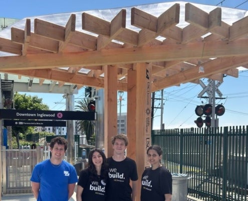 Four students stand underneath a wooden shade structure at the Downtown-Inglewood Metro station