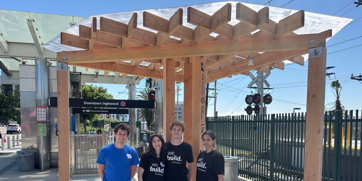 Four students stand underneath a wooden shade structure at the Downtown-Inglewood Metro station