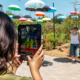 A person uses a tablet to capture a thermal image of two girls standing outdoors under a shade installation of floating, colorful umbrellas.