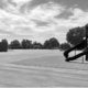 Unshaded playground with two slides and a large paved surface, with trees and buildings in the background.