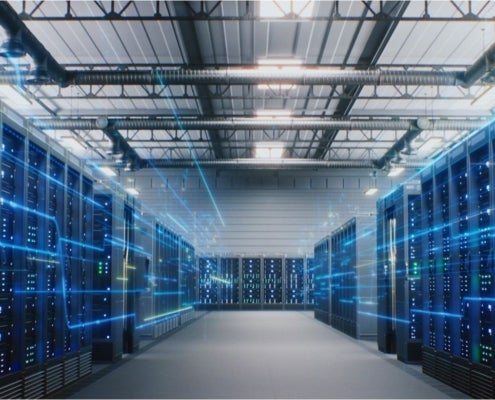 Server room with rows of illuminated computer servers, overhead ventilation ducts and blue digital light effects.