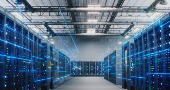Server room with rows of illuminated computer servers, overhead ventilation ducts and blue digital light effects.