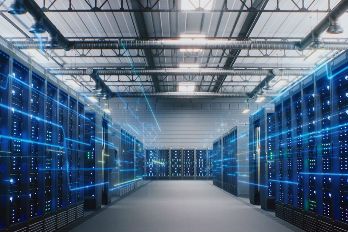 Server room with rows of illuminated computer servers, overhead ventilation ducts and blue digital light effects.